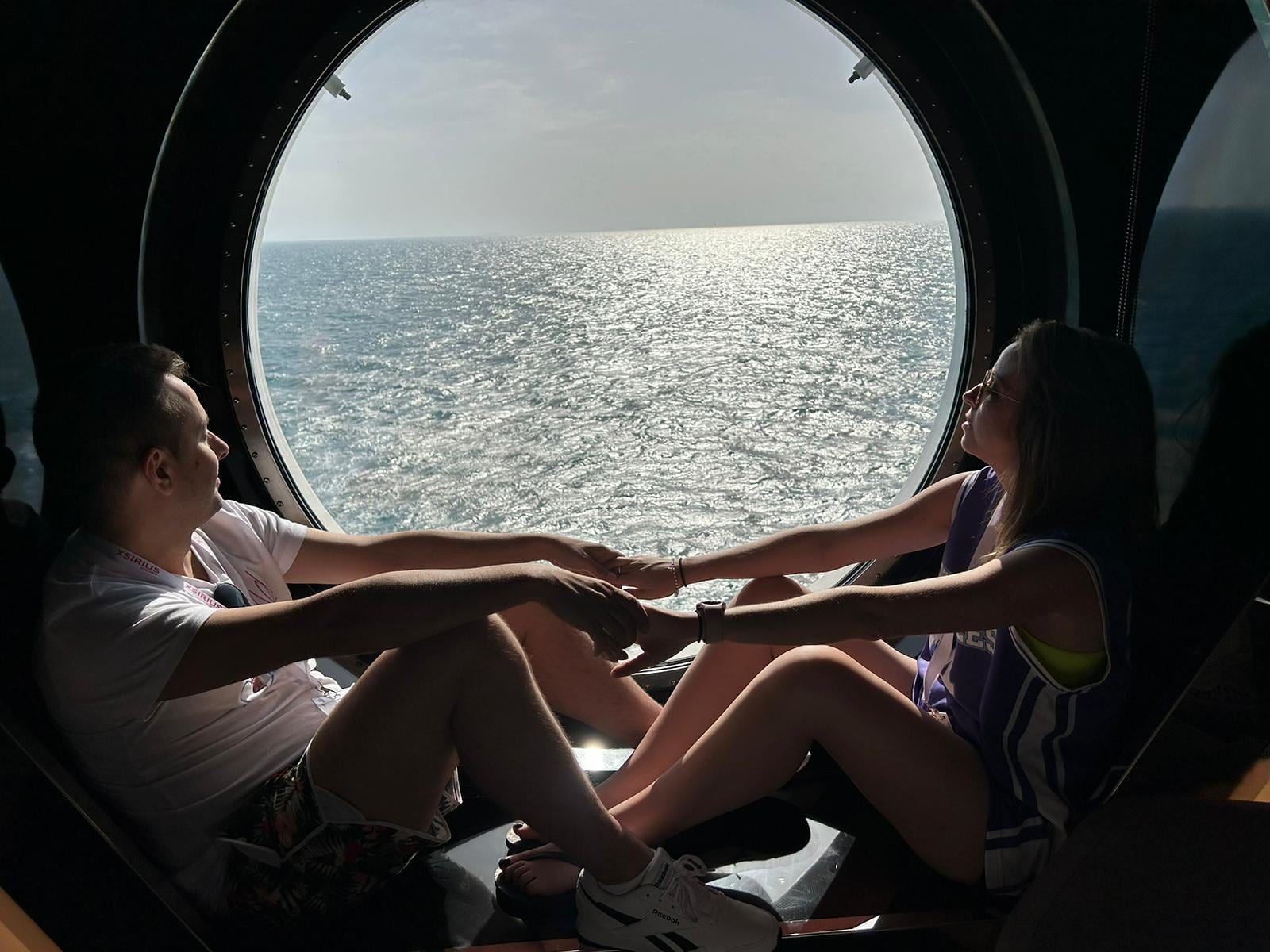 Dos viajeros del grupo mirando el mar desde un gran ojo de buey del barco